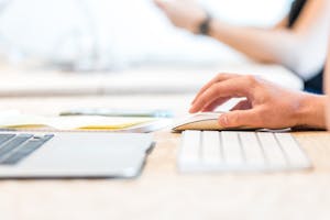 A person working at a laptop with a wireless mouse and keyboard in a bright office setting.